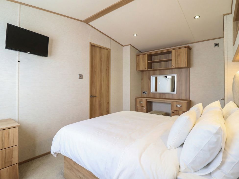 A bedroom with a bed, television, and dresser at 23 Gull Court in Porthmadog