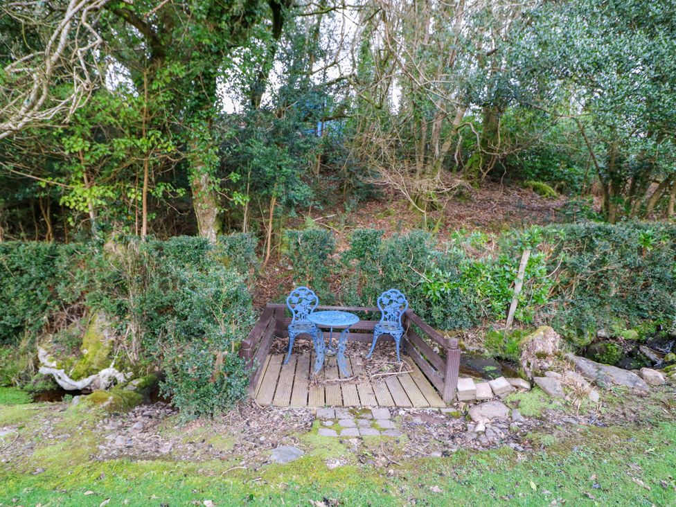 A table and chair next to a stream at Lugdine Lodge in Glengarriff