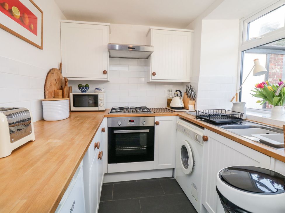 A kitchen with a gas stove, microwave, and sink at Burnside Cottage in Grange-Over-Sands