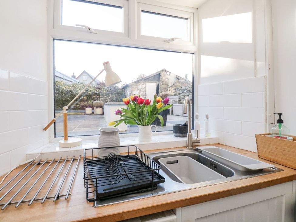 A kitchen sink with a window and flowers at Burnside Cottage in Grange-Over-Sands