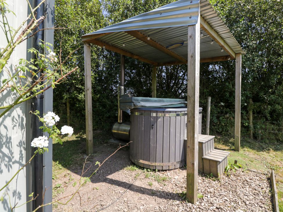 A hot tub under a canopy in a garden at Daisy Shepherd's Hut South Molton