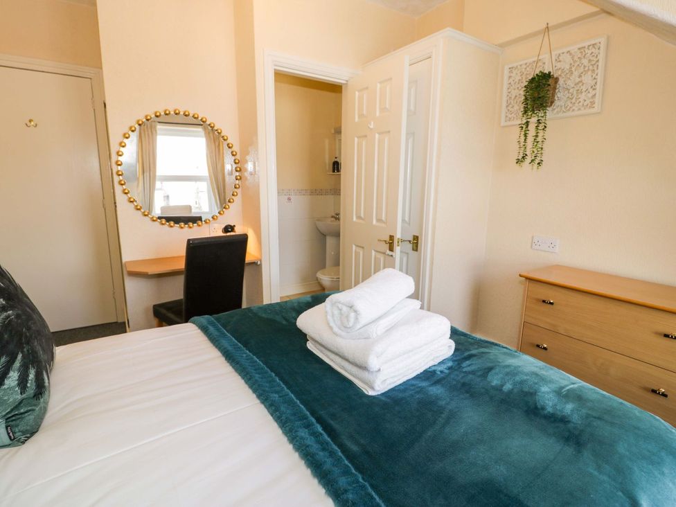 A bedroom with a bed, towels, mirror, desk, and chair at The Causeway in Llandudno