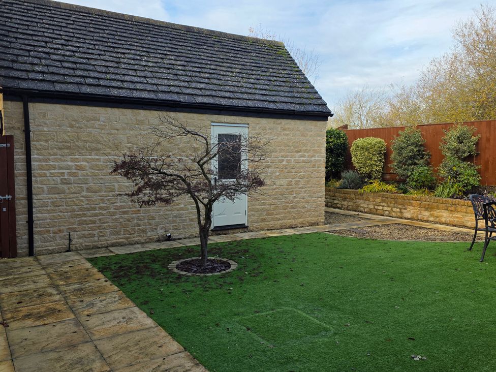 A garden with a tree, grass, and a stone wall at Spacious 4-Bedroom Cotswold Home in Lechlade