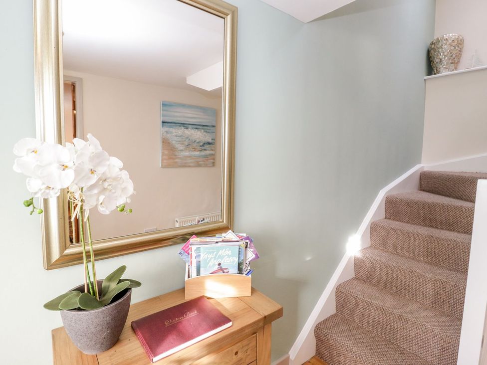 A hallway with a mirror, a plant, magazines, and a staircase at Eryri View Retreat