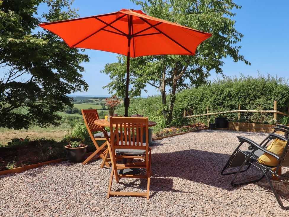 A garden area with a table and chairs under an umbrella at Nelli Lodge at Mile End in Crediton