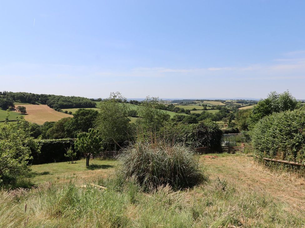 A garden with grass and trees overlooking hills at Nelli Lodge at Mile End, Crediton