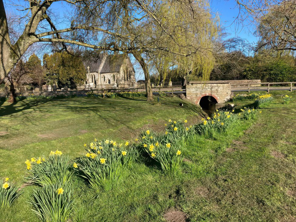 A church surrounded by trees and daffodils near a bridge at Bumble Bee Lodge Muston