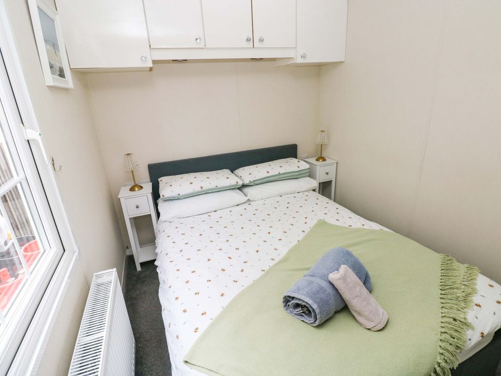 A bedroom with a bed, nightstands, and towels at Meadows Farm Lodge in Gorseinon