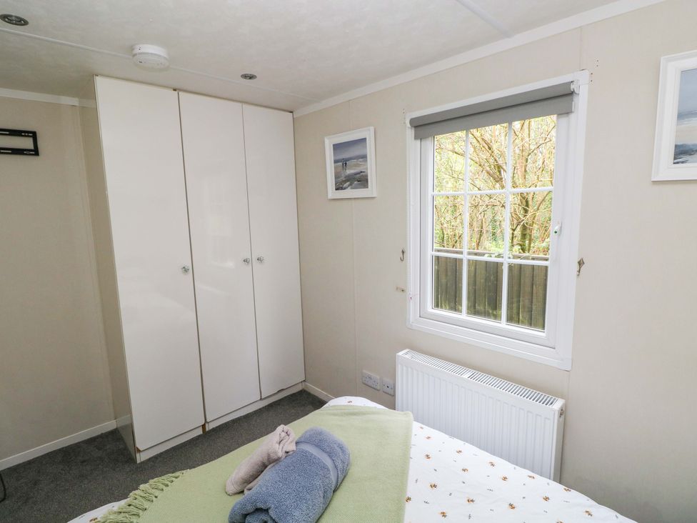 A bedroom with a wardrobe and window at Meadows Farm Lodge in Gorseinon