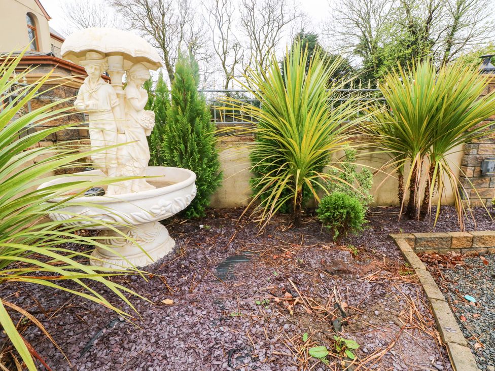 A garden with a fountain and palm plants at Meadows Farm Lodge in Gorseinon