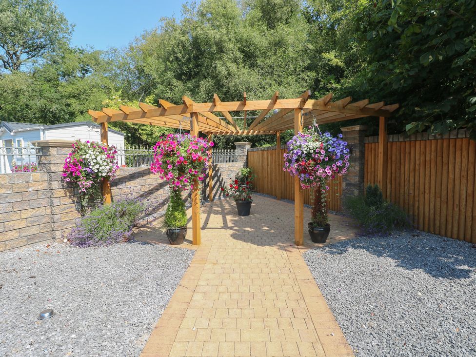 A garden with a pergola and hanging baskets at Meadows Farm Lodge in Gorseinon
