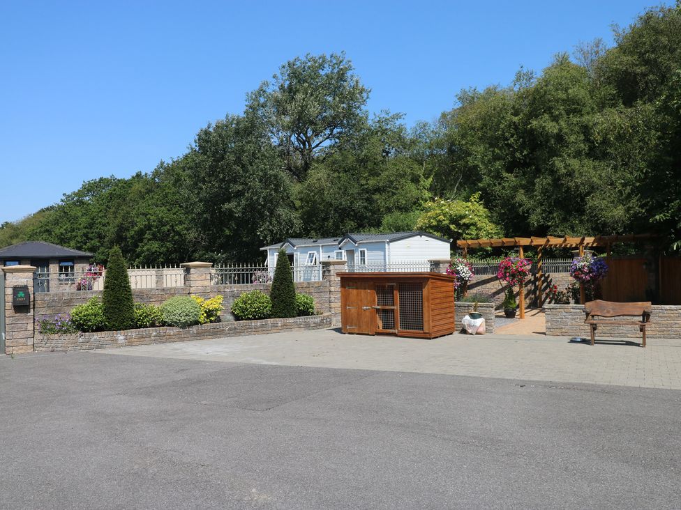 An outdoor area with a caravan and a wooden pet enclosure at Meadows Farm Lodge Gorseinon