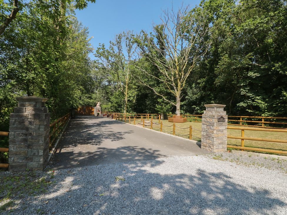 A gravel driveway leading through trees and a fence at Meadows Farm Lodge in Gorseinon