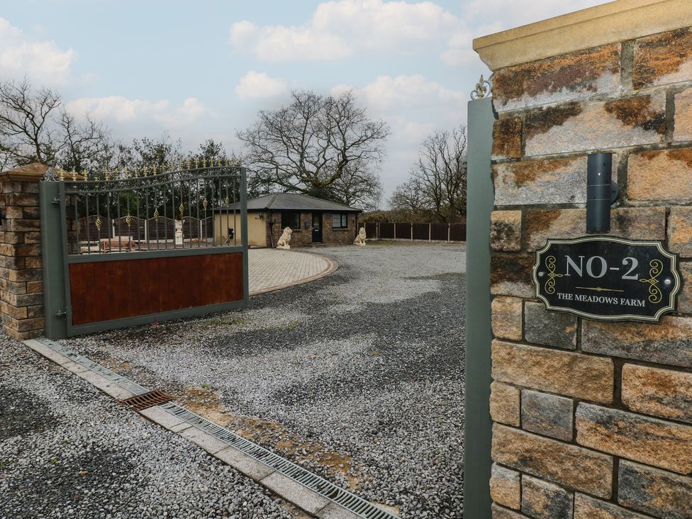 A gated entrance with a stone wall and gravel driveway at No-2 The Meadows Farm Swansea