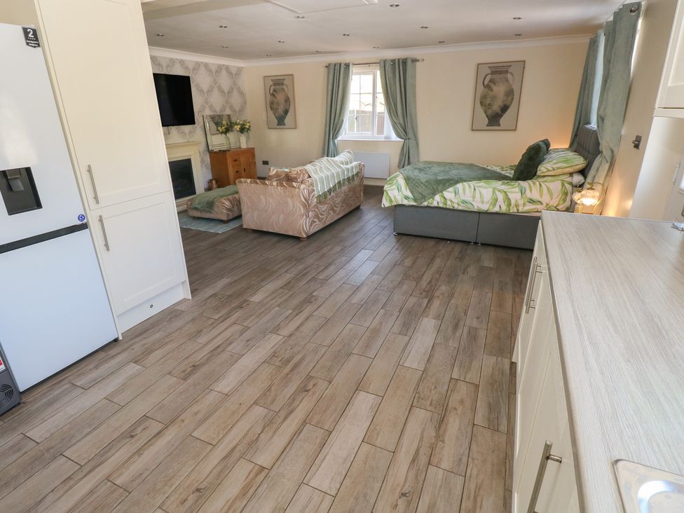 A studio apartment with a refrigerator, sofa, bed, and television at Annexe @ Meadows Farm, Gorseinon