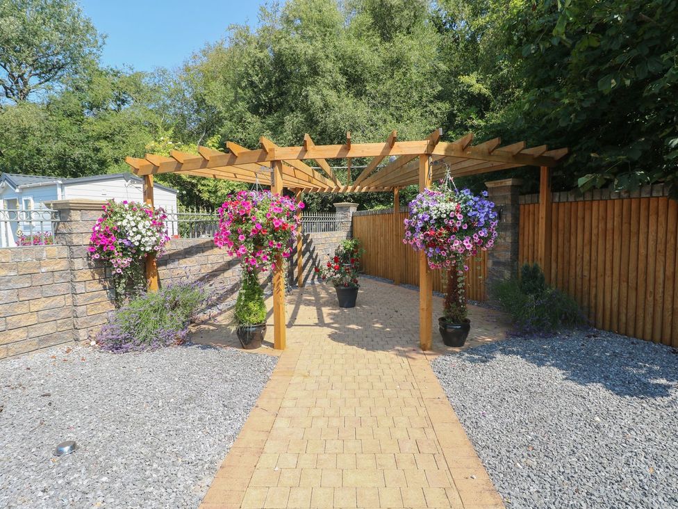 A garden with a wooden pergola and hanging flower pots at Annexe @ Meadows Farm, Gorseinon