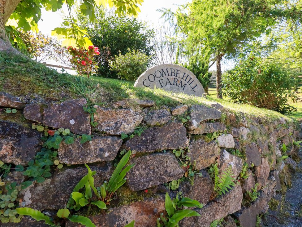 A stone wall with a sign reading Coombe Hill Farm in an outdoor area