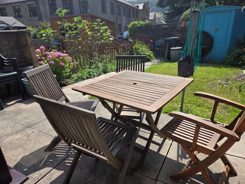 A garden with a wooden table and chairs at Beckside Cottage in Hebden Bridge