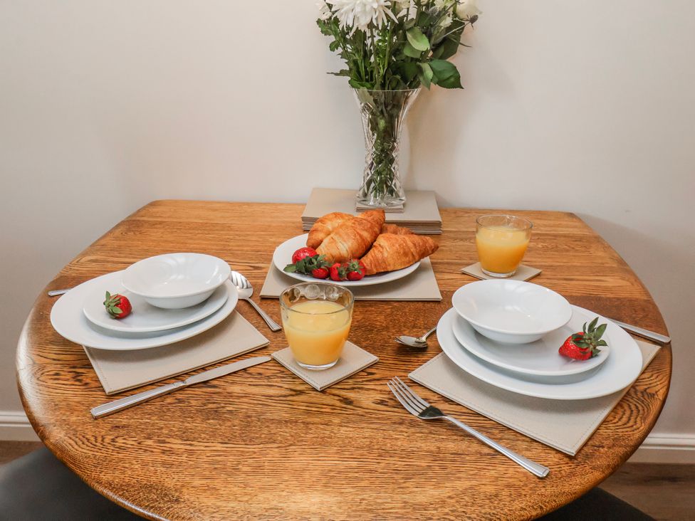 A dining table set with plates, bowls, croissants, strawberries, and orange juice at Holly Cottage in Whitby