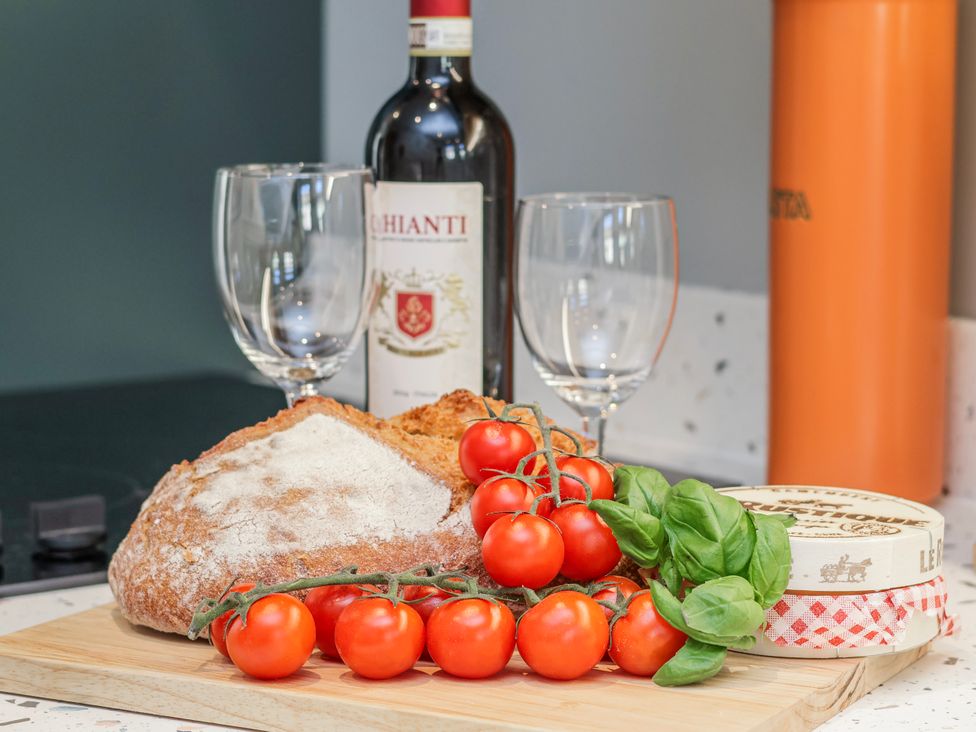 A kitchen countertop with bread, tomatoes, wine, cheese, and glasses at Holly Cottage in Whitby