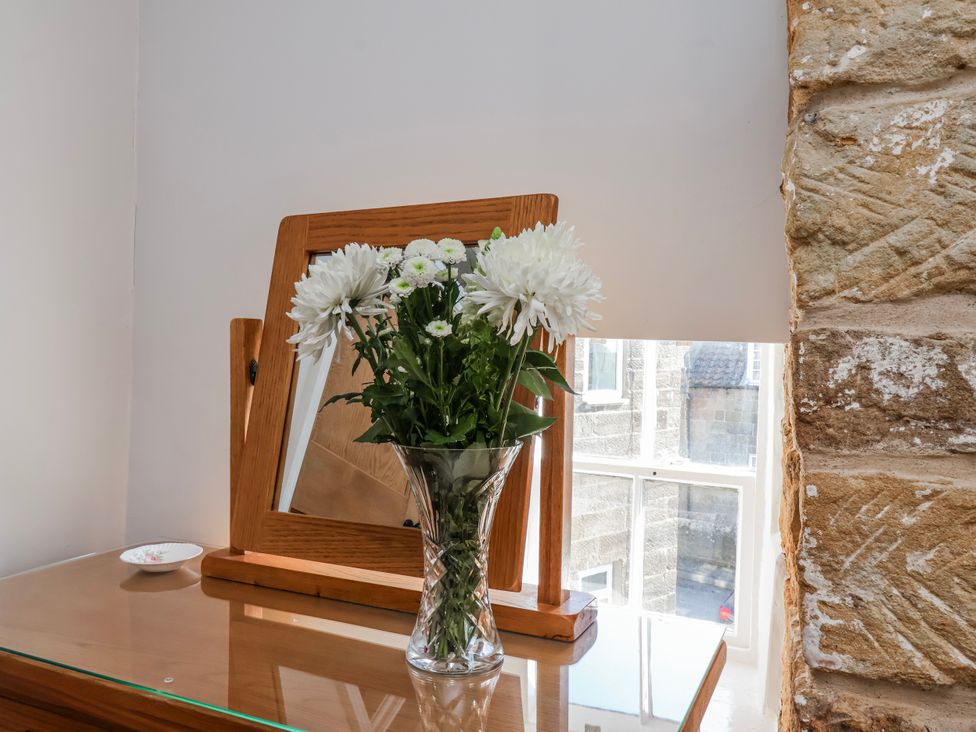 A flower vase on a wooden dresser with a mirror at Holly Cottage in Whitby