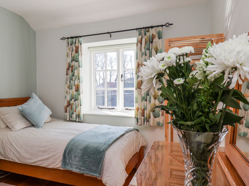 A bedroom with a bed and flowers on the nightstand at Holly Cottage in Whitby