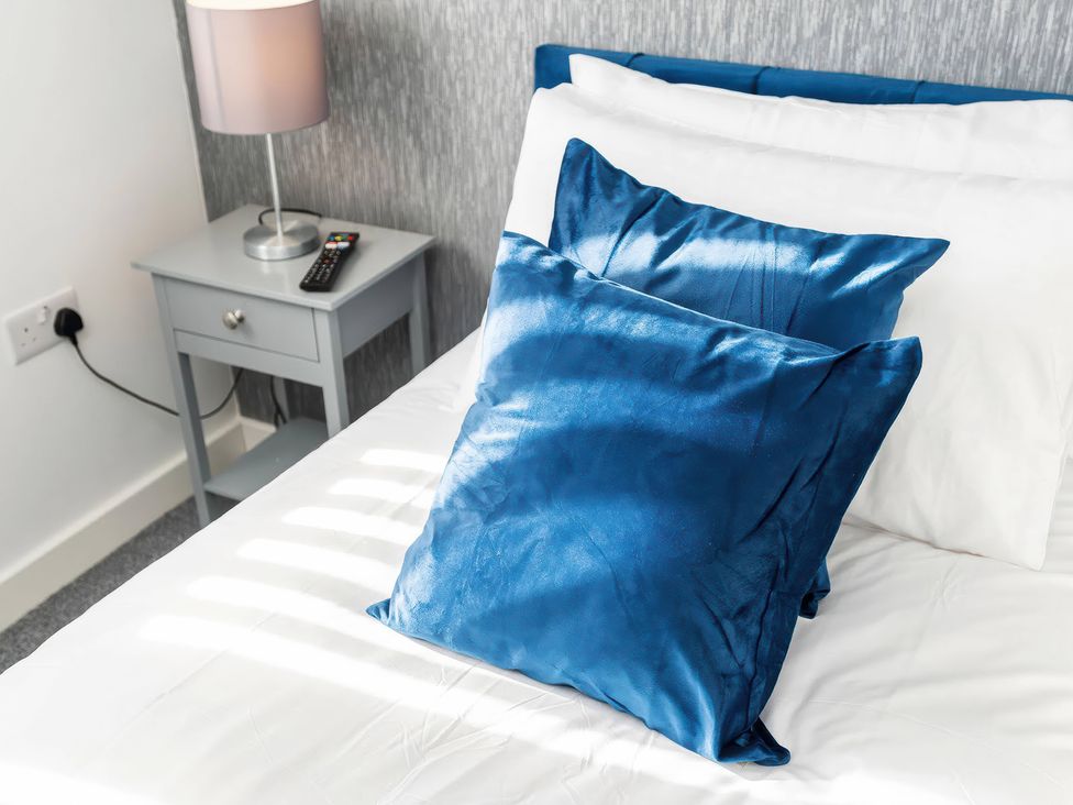 A bed with blue cushions and a side table with a lamp and remote control at 59 Eagle Drive in Grimsby