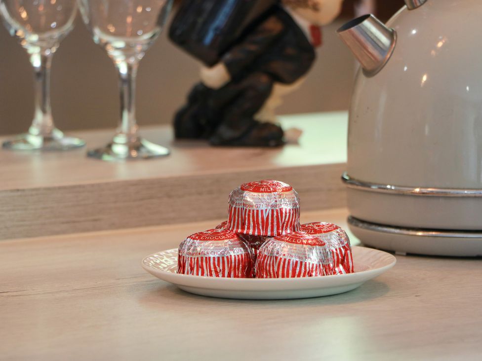 A plate with chocolates next to a kettle and wine glasses at Crown Cottage in Newmills near Cairneyhill