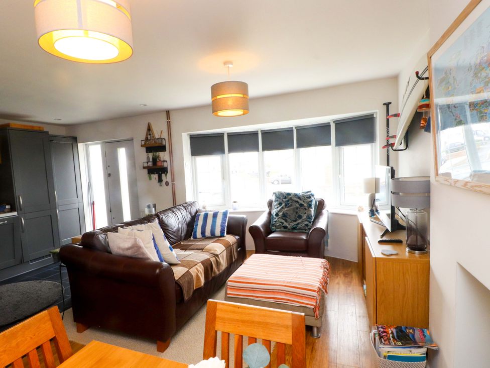 A living room with a sofa, armchair, coffee table, and television at 7 Sisial Y Mor in Rhosneigr