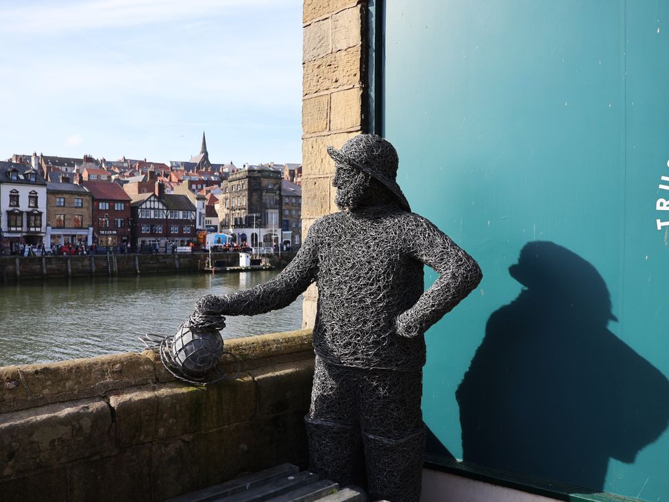 A statue holding a lantern near the water at Bishop's Cottage in Whitby