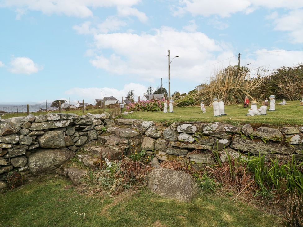 A garden with a stone wall and decorative figures at Happy Landing in Harlech