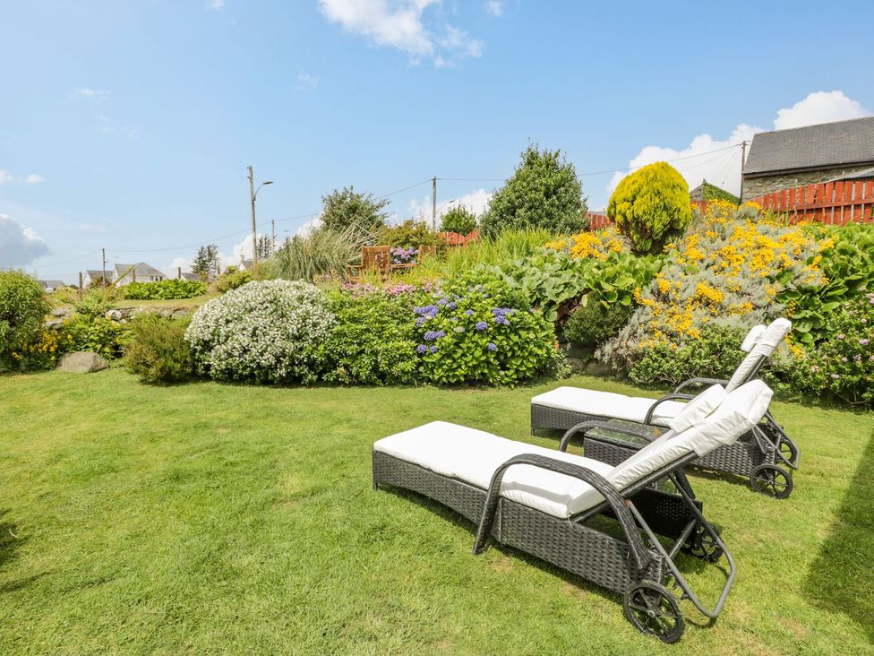 A garden with lounge chairs and a flower bed at Happy Landing in Harlech