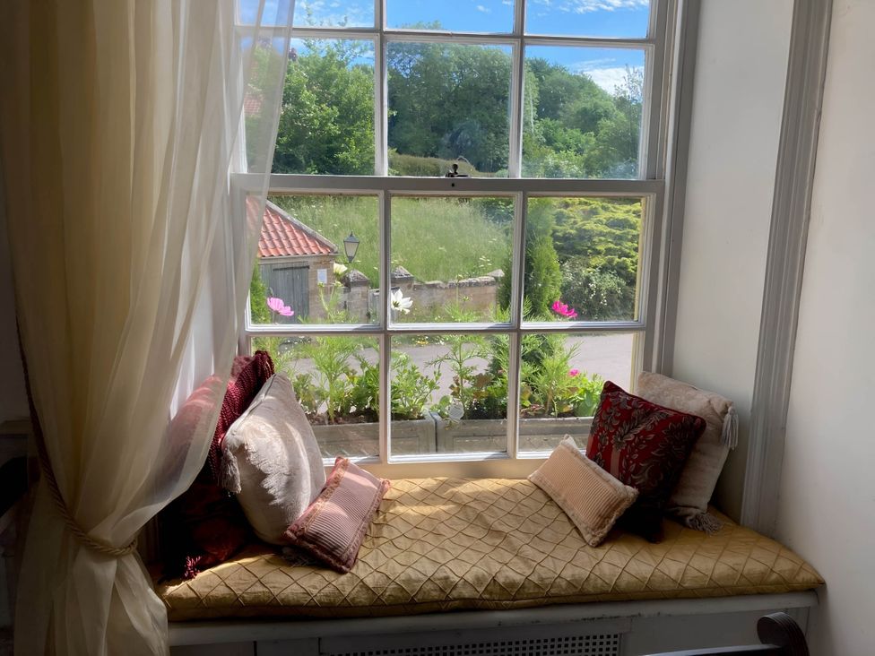 A window seat with cushions and a view of flowers at Groves Hall Garden Apartment Whitby