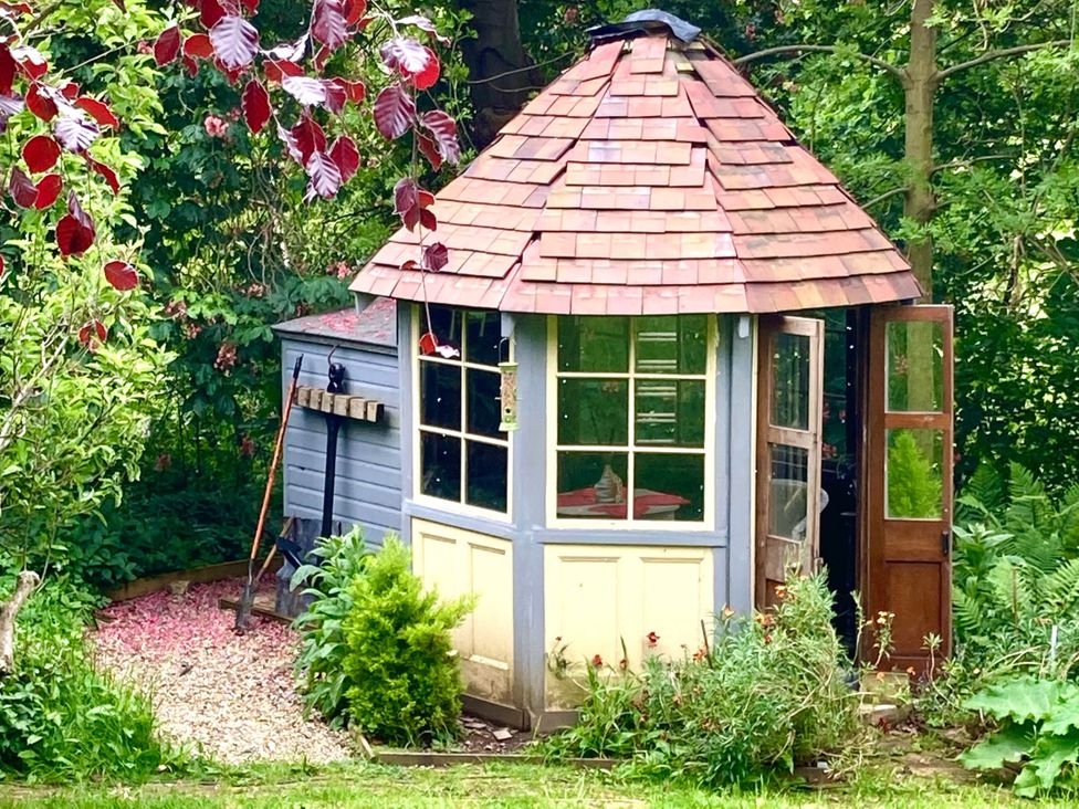 A garden shed with a conical roof and open door in a garden at Groves Hall Garden Apartment Whitby