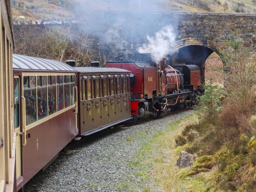 A steam locomotive passing under a bridge in the countryside at Bodorwel Cottage Penrhyndeudraeth