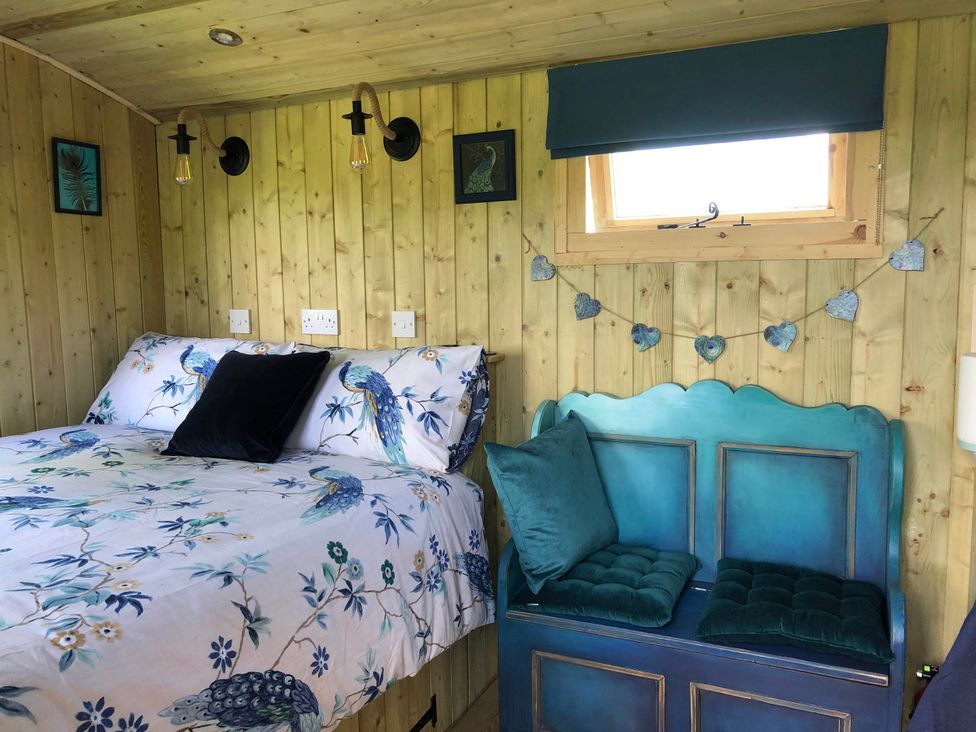 A bedroom with a bed and bench seating at The Peacock Shepherds Hut at Hafoty Boeth, Corwen