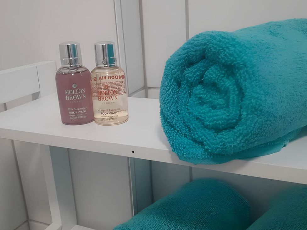 A bathroom shelf with body wash bottles and a rolled towel at 1-Bed House, Sleeps 4, Free Parking