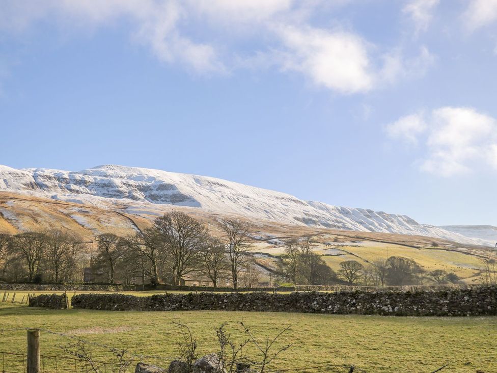 A mountain covered in snow with trees and a stone wall at Orcaber Farm Retreat in Lancaster