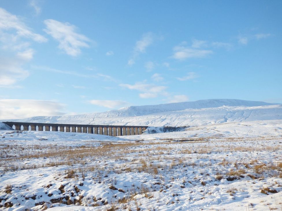 A bridge over snow-covered ground with mountains in the background at Orcaber Farm Barn Lancaster
