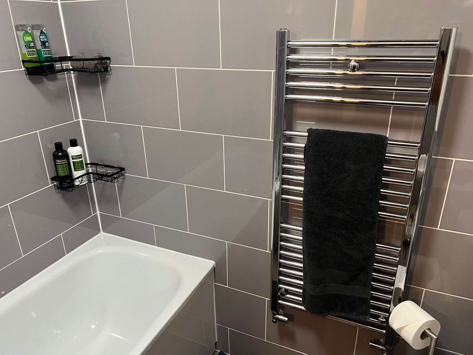 A bathroom with a bathtub, towel radiator, and shelves with toiletries at Seaside Cottage Escape in Paignton