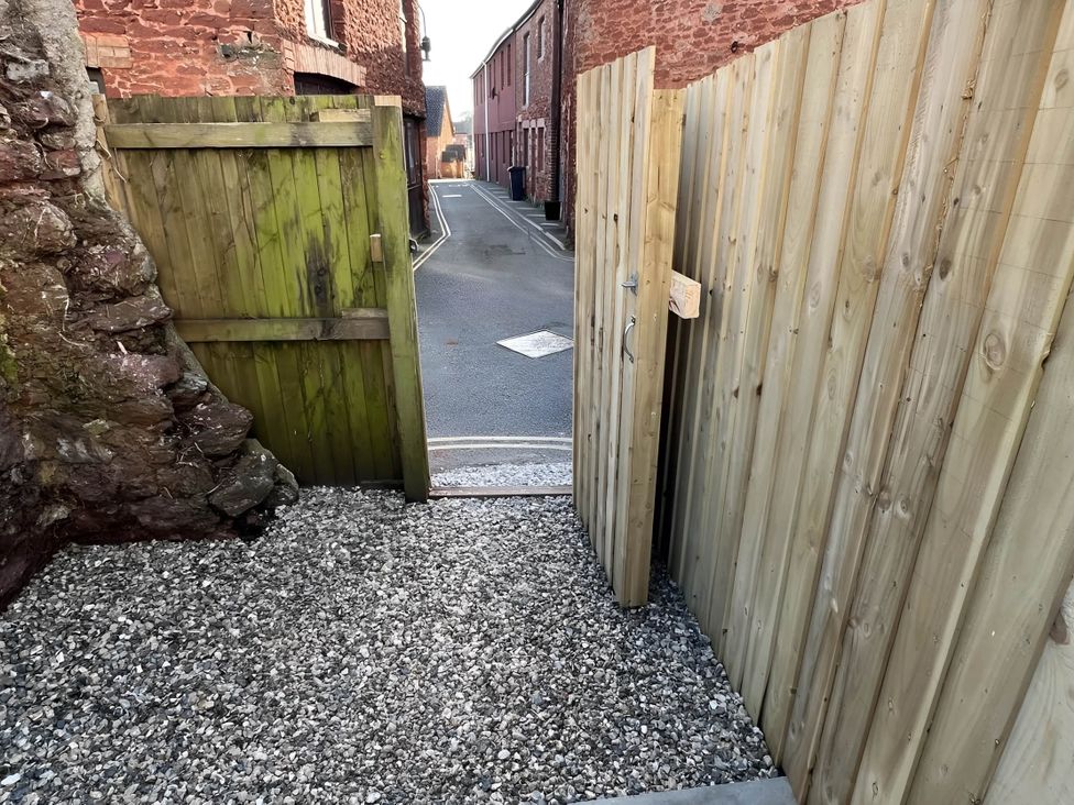 A view from a gravel area through a wooden gate towards a street at Seaside Cottage Escape in Paignton