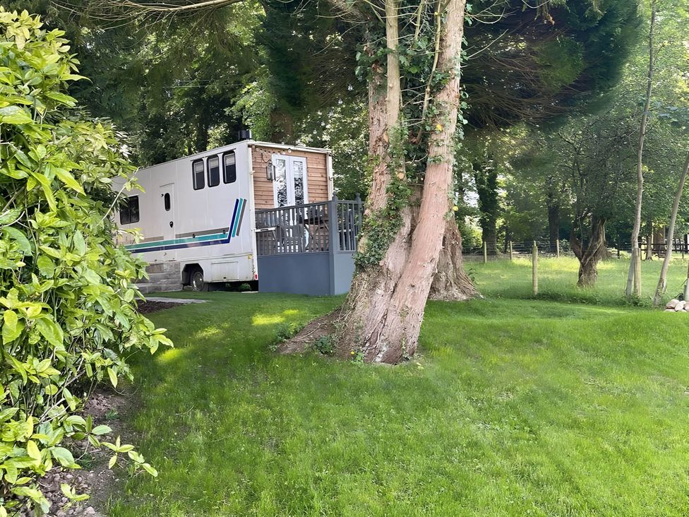 A motorhome with a deck surrounded by trees and grass at Dobbin the horse box in The Lake District Cockermouth