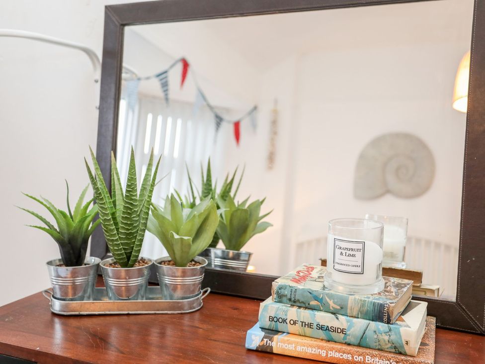 A table with a mirror, potted plants, a candle, and books at Rhiwlas Rhosneigr
