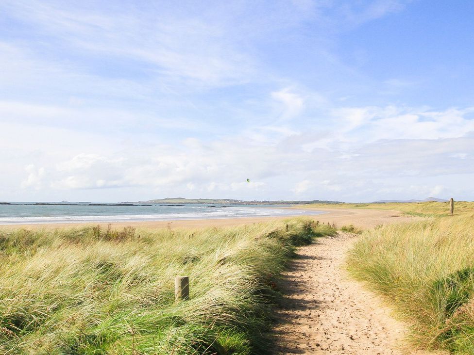 A beach with a sandy path and grass near the water at Rhiwlas in Rhosneigr