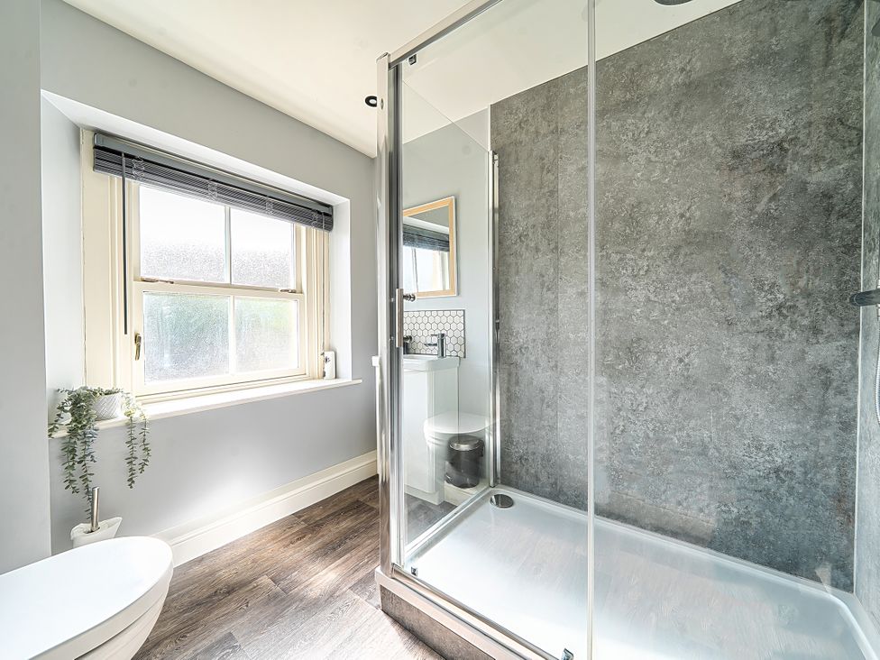 A bathroom with a shower, toilet, sink, and window at Cosy Apartment above Village Pub in Taddington