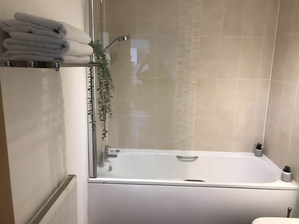 A bathroom with a bathtub, showerhead, towels and plants at 2-Bed Apartment Sleeps 4 with Garden