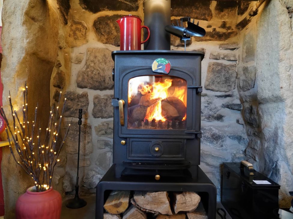 A wood stove with logs and a kettle in a living room at Traditional 2 Bedroom Cottage in Eyam, Hope Valley