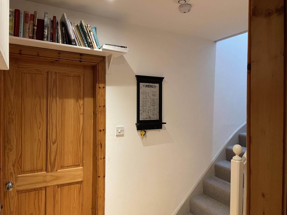 A hallway with a wooden door and books on a shelf at 1 Keepers Cottage, Skeabost Bridge, Isle Of Skye