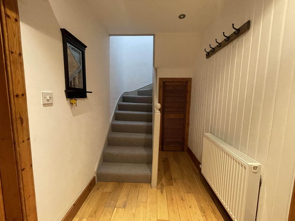 A hallway with a staircase and coat hooks at 1 Keepers Cottage, Skeabost Bridge, Isle Of Skye