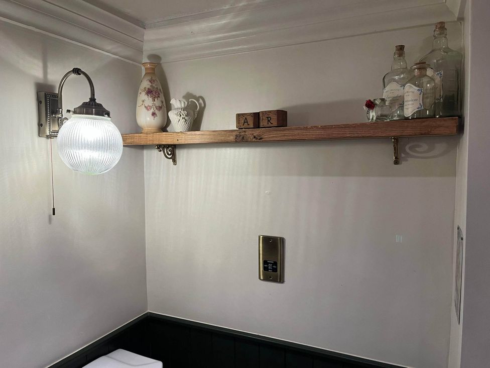 A shelf with decorative items and a light in a bathroom at Quiet cottage on the rural edge of Brixham